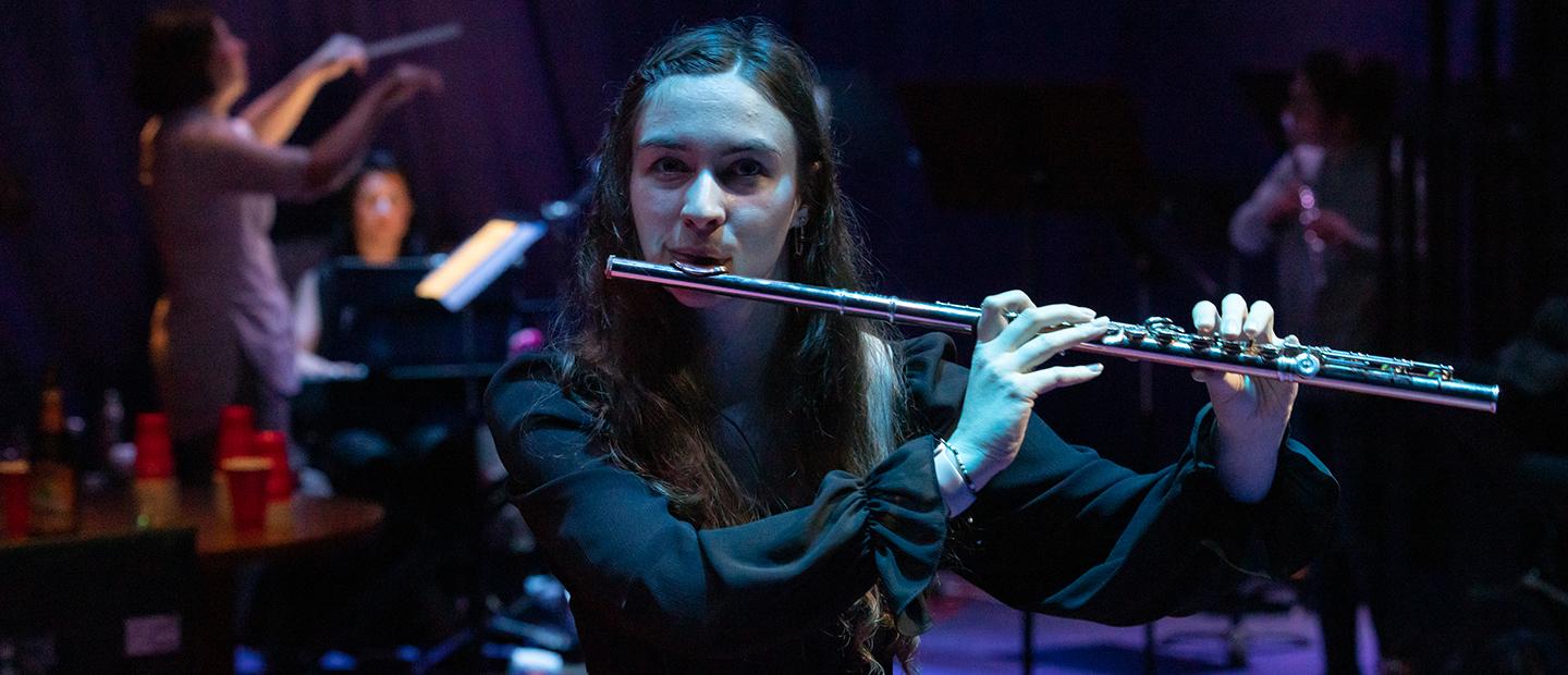 Female student playing the flute on stage, looking directly into the camera